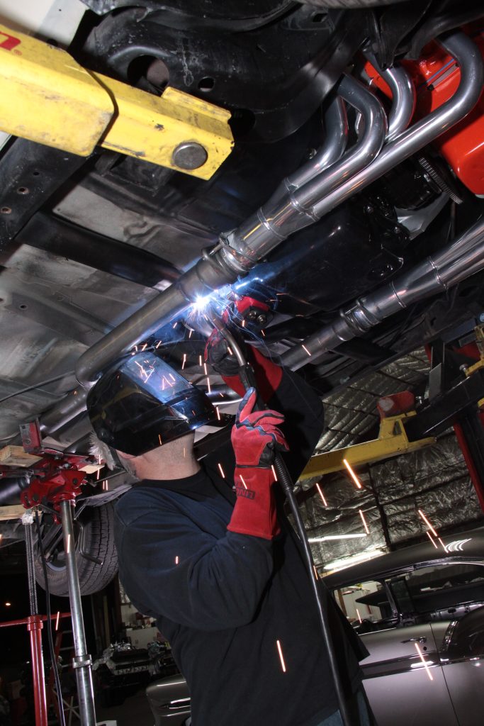 man welding exhaust tubing under a car