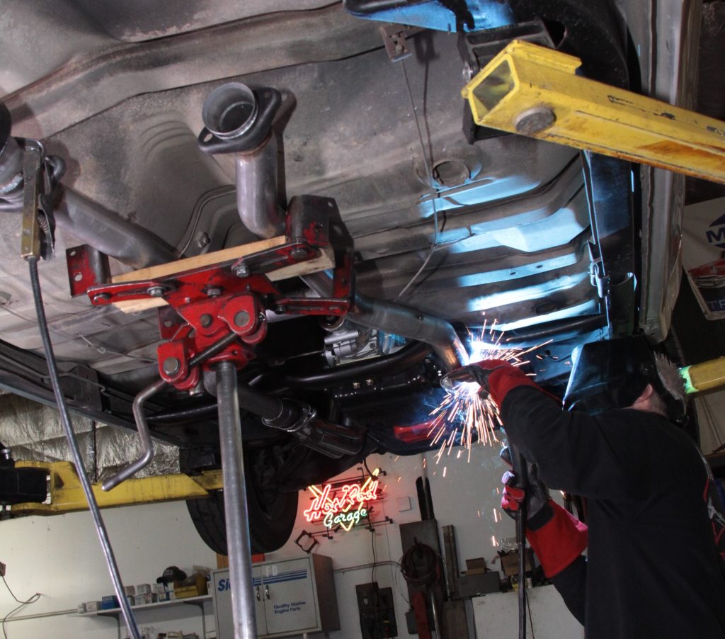 man welding an exhaust system under a classic car