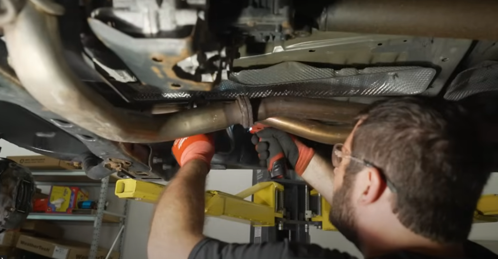 man removing a factory exhaust system under a truck