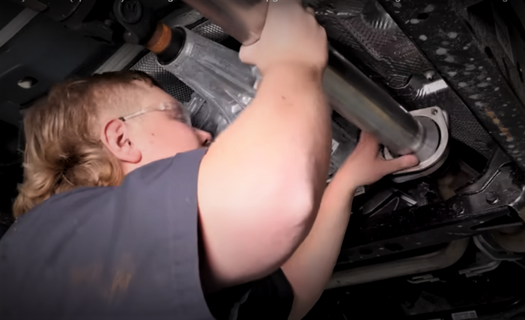 man fitting an exhaust pipe under a truck