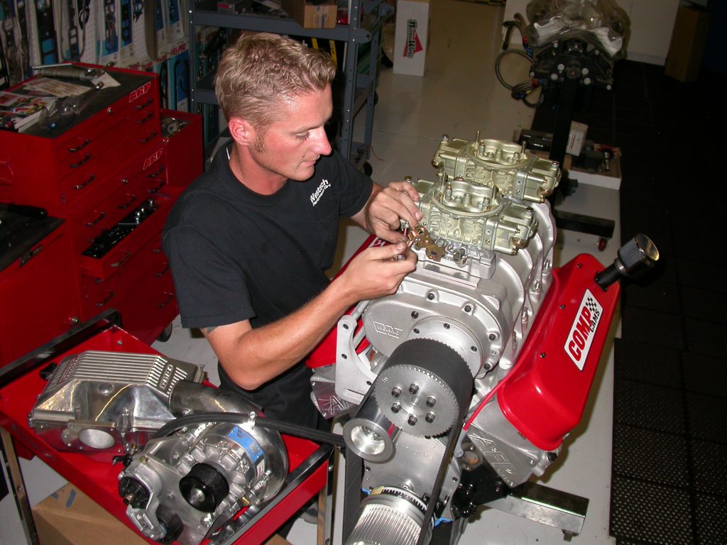 man installing carburetors atop a supercharged v8 engine