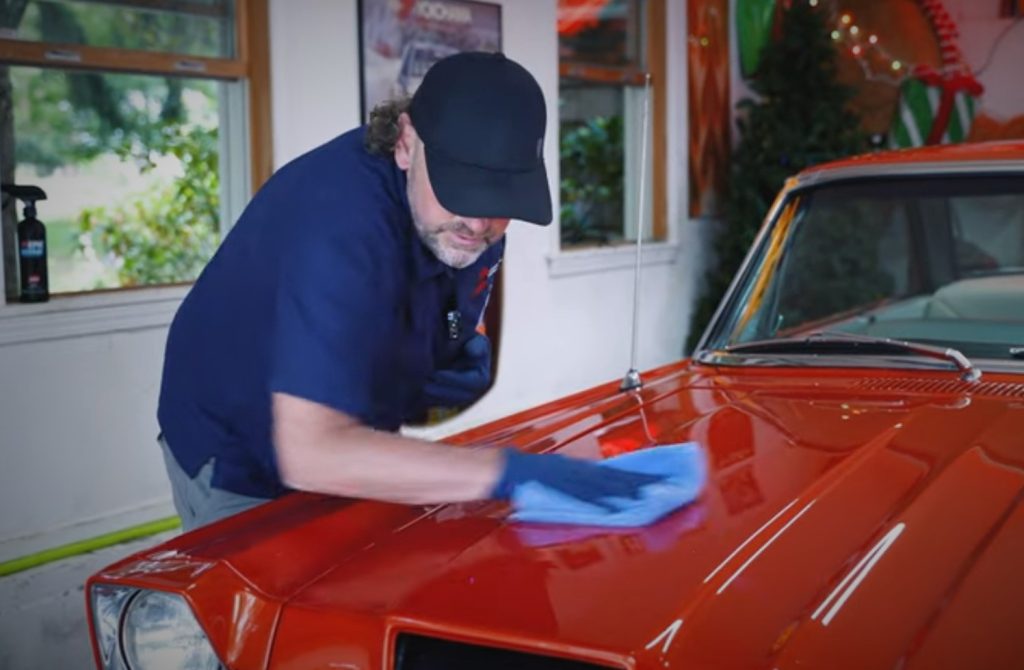 man wiping clean rag down hood of muscle car