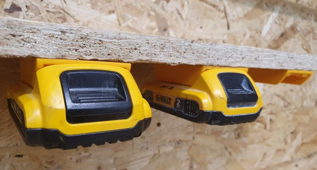 power tool batteries clipped to a piece of wood in a shop