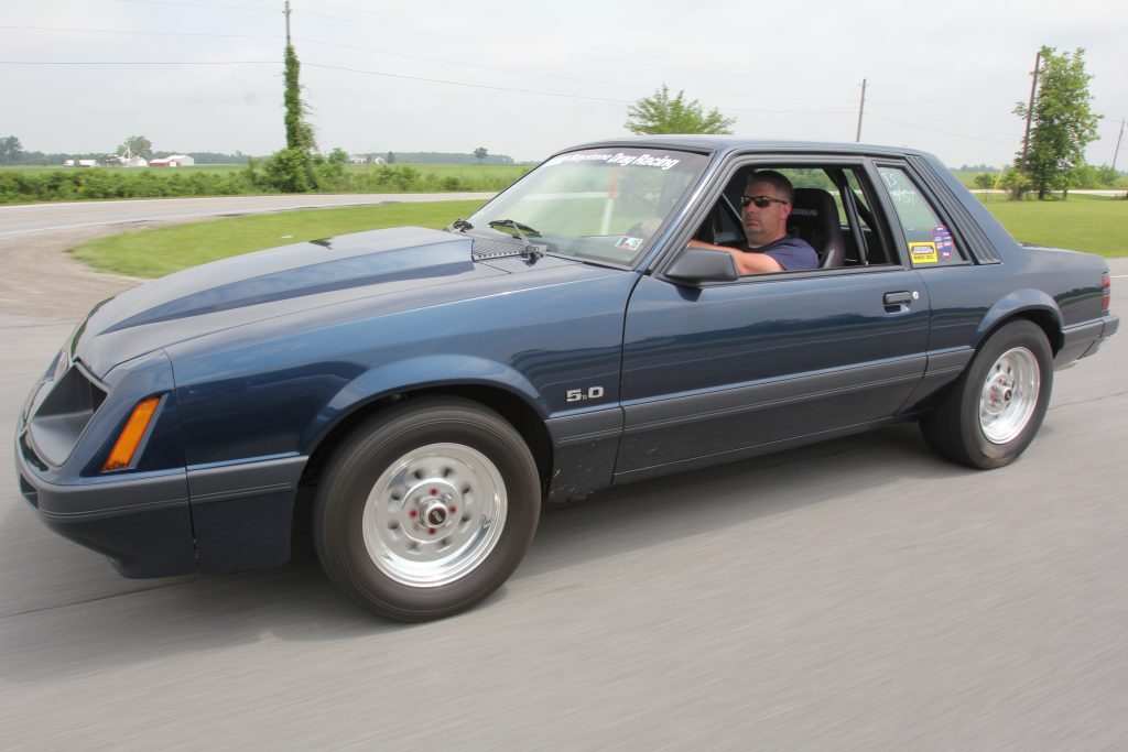 man driving a foxbody mustang on a road