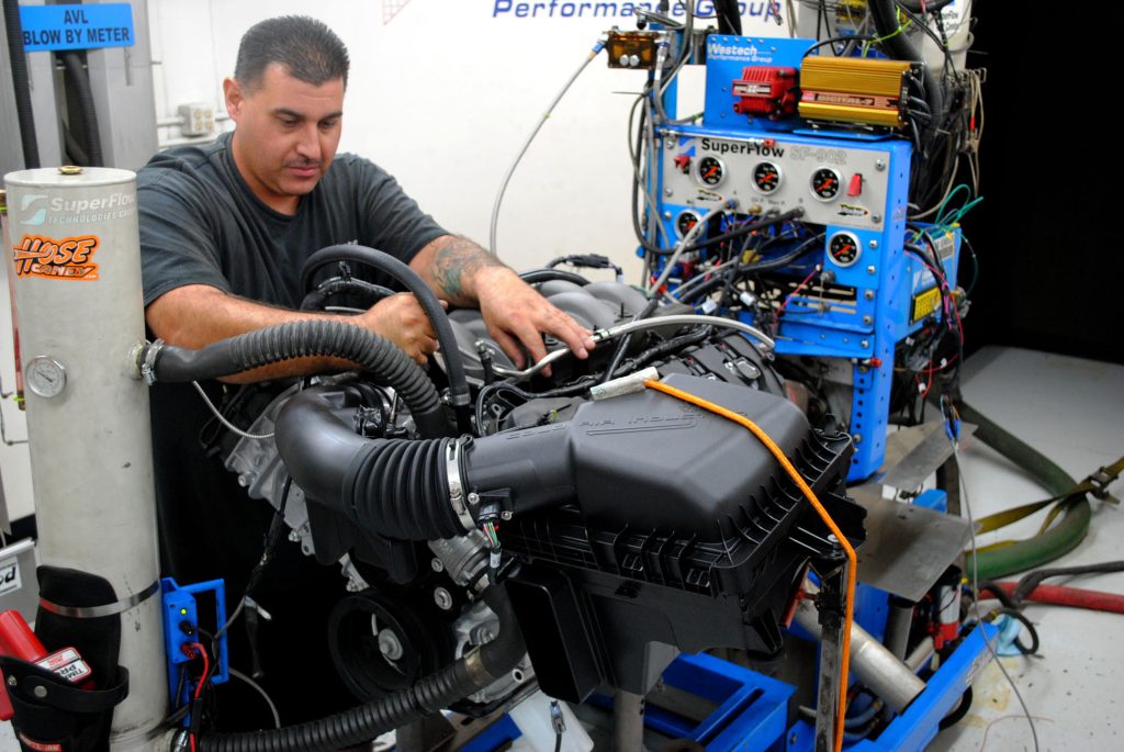 man installing manifold onto a coyote engine on dyno