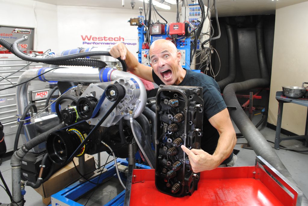 man with cylinder head next to a supercharger